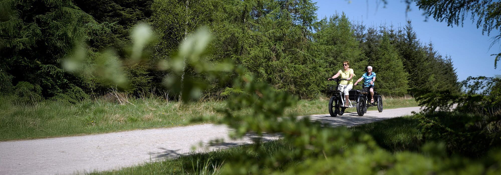 A senior couple riding electric tricycles on a trail path in a forest.