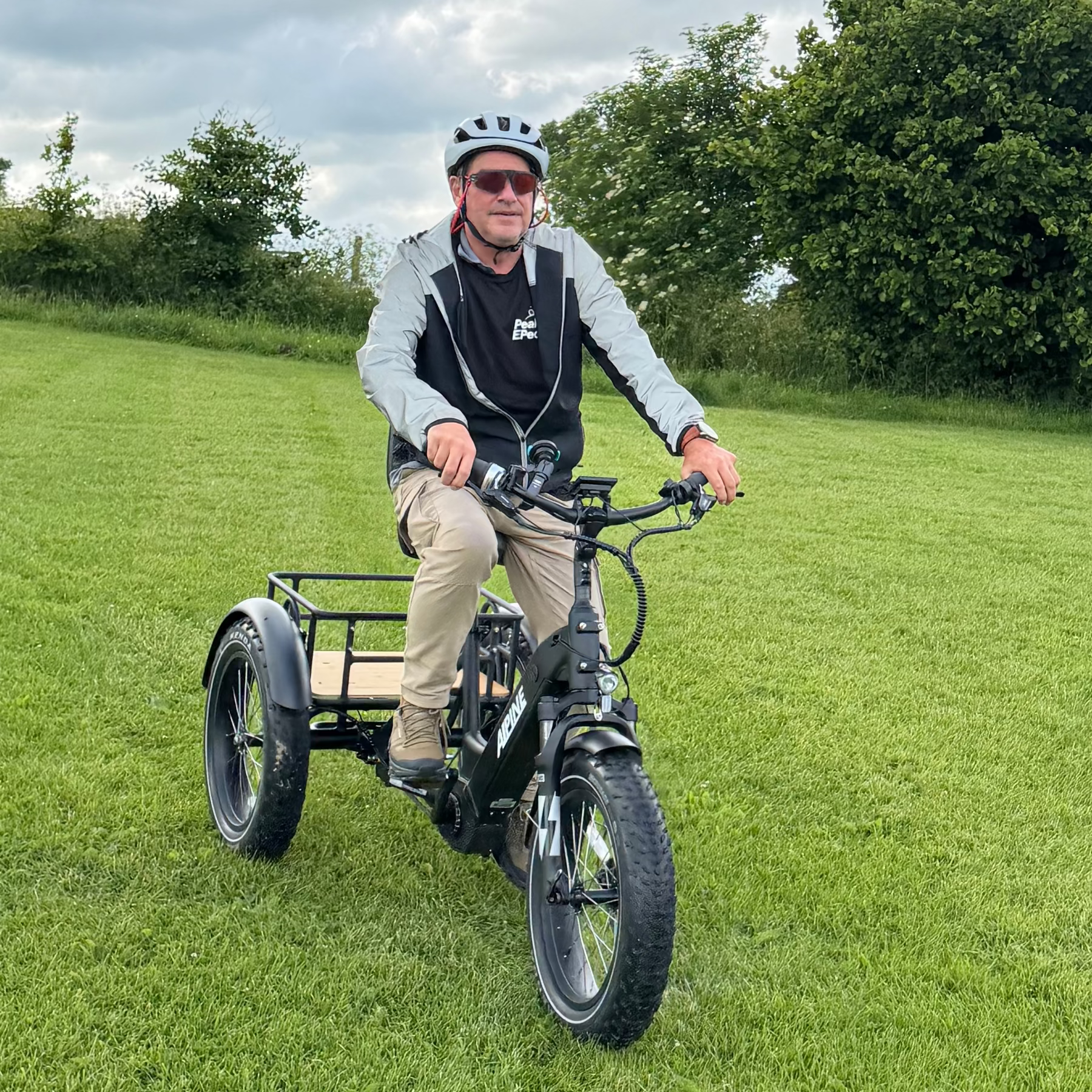 Man riding a tricycle in a grassy field with trees in the background