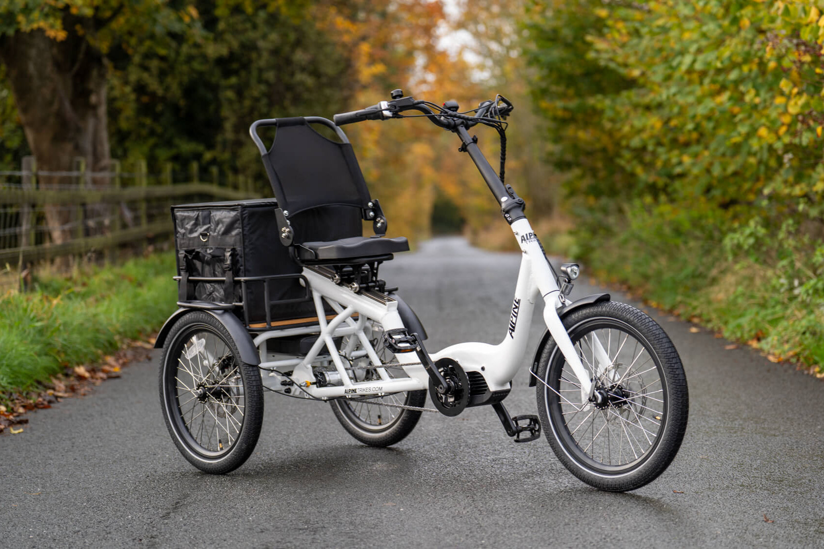 White electric tricycle with a black seat on a road surrounded by trees and grass.