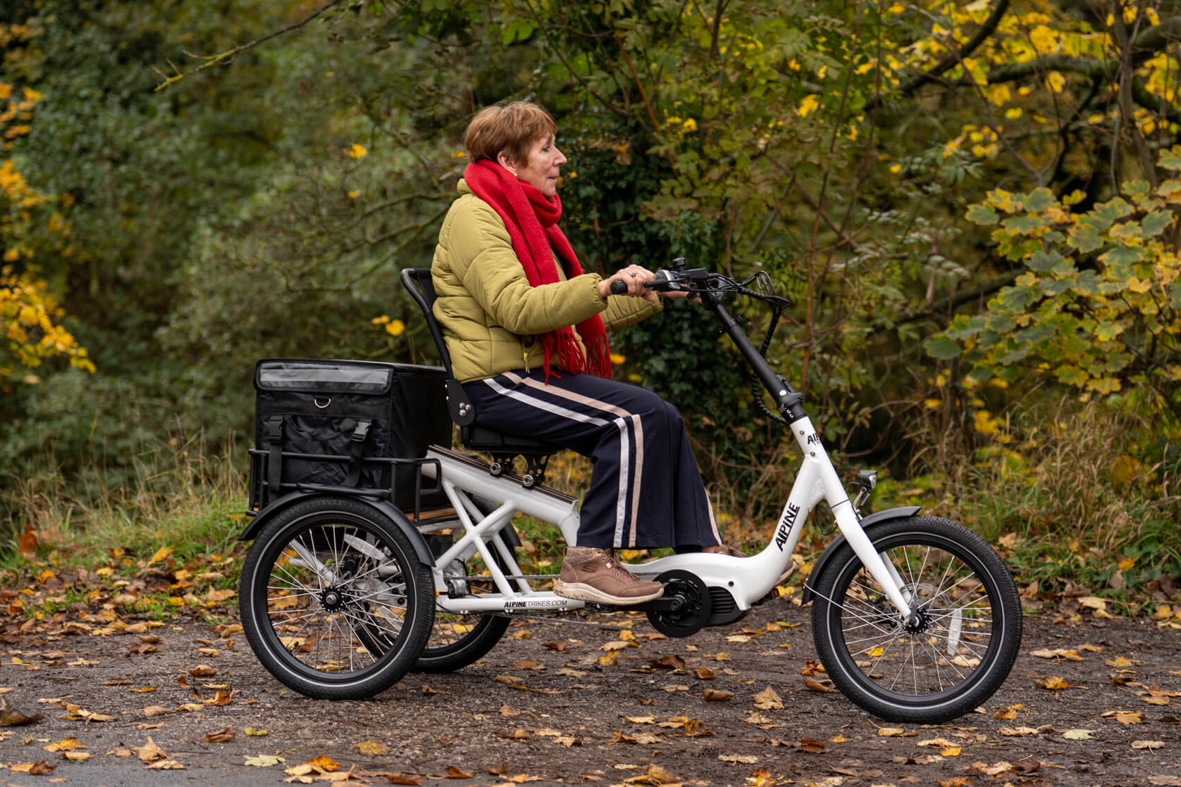 Person riding a white electric tricycle in a forest setting with autumn leaves.