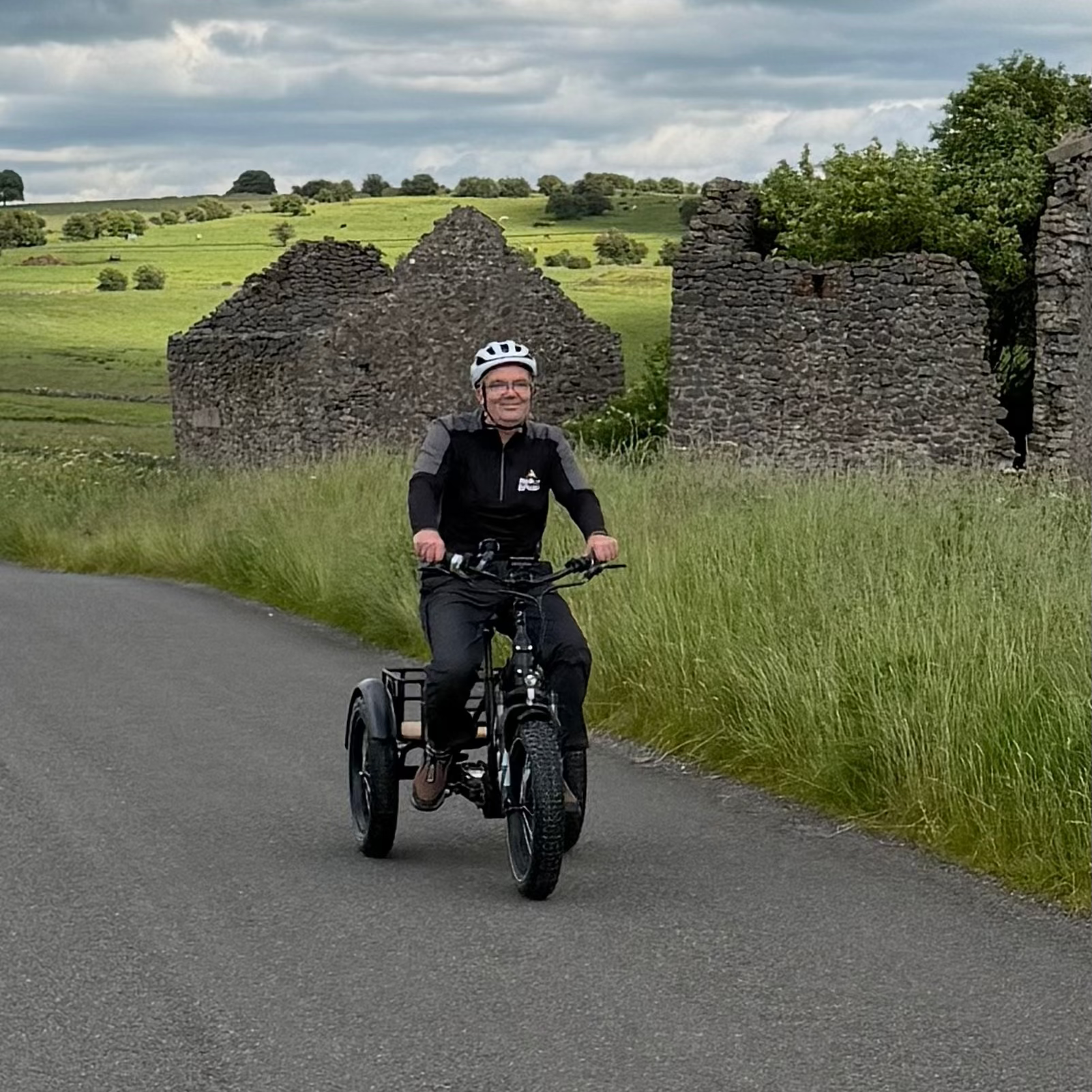 Person riding a trike on a road with stone ruins and green fields in the background